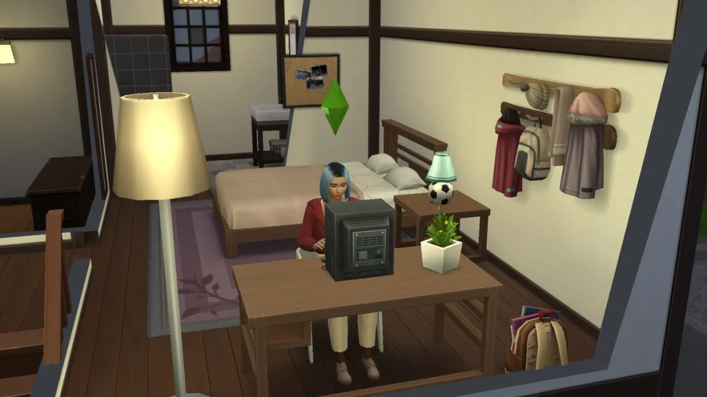 Kaori Nishidake in The Sims 4 sat at a desk using a PC in her home in Mt Komorebi. It's a tatami-style room decorated with postcards and trinkets.