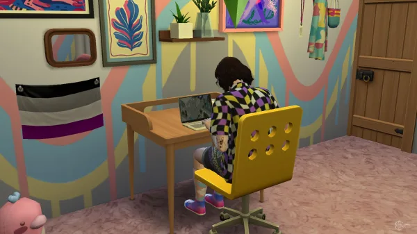 A Sim sat playing video games at a laptop on a desk in a very brightly coloured room. There's pride merch and furniture everywhere, including a massive gallery wall with an Asexual pride flag. The Sim is sat at a yellow chair wearing a yellow and purple shirt.