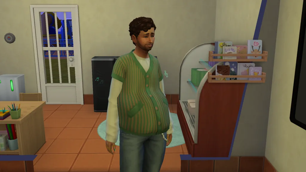 A pregnant Sim in The Sims 4 stood in a house with a chilled shelf and toddler books behind him. He's wearing blue jeans and a green cardigan.