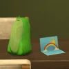 A papier-mache frog on a table next to a pop-up rainbow celebration card. in The Sims 4: Adventure Awaits.