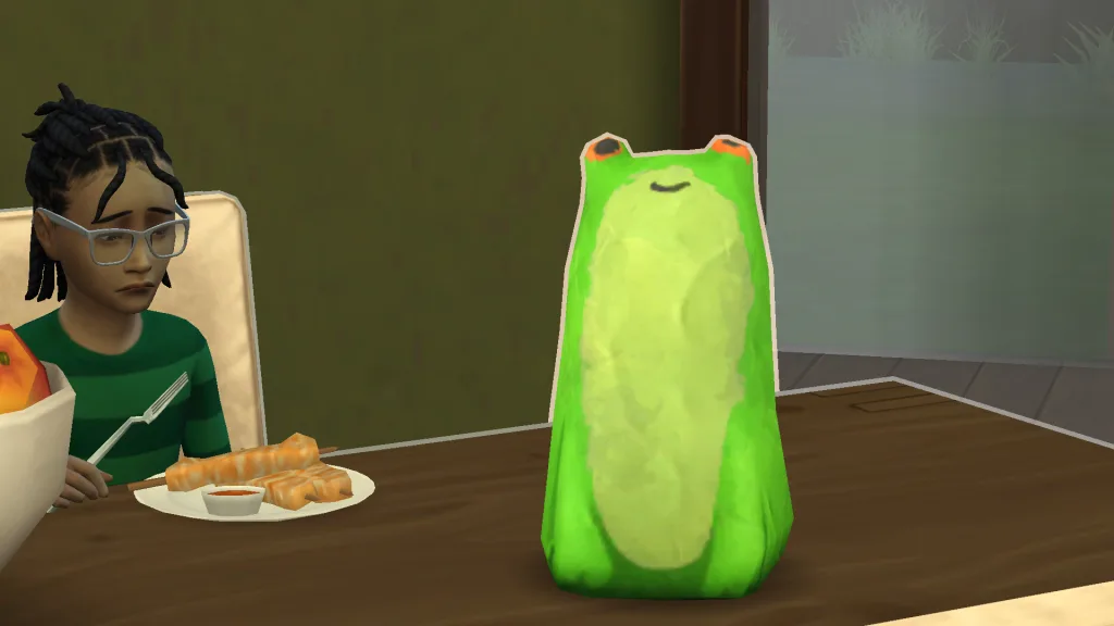 A funky looking papier mache frog with a dorky expression on a table. A child sits next to it eating dinner while looking sad.