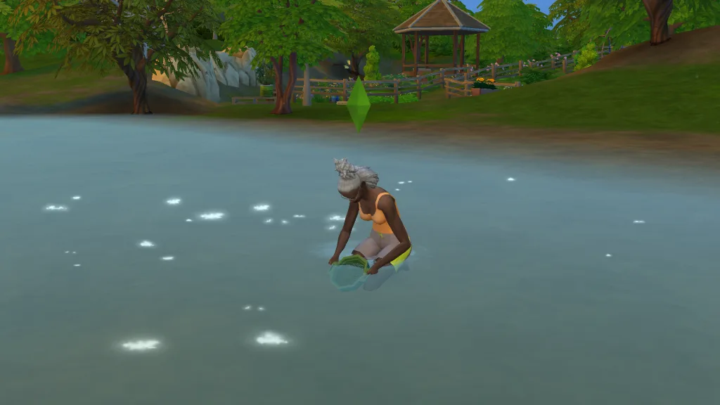 A Sim crystal panning in the shallows of the riverbank in The Sims 4: Adventure Awaits with the public garden in view behind her.